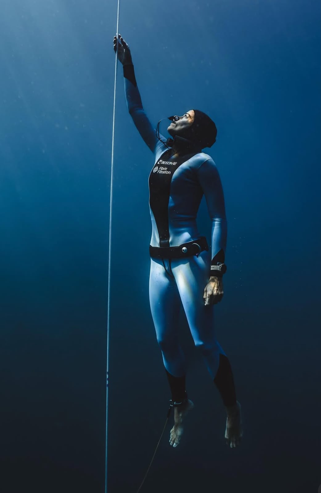 Tania Panés underwater holding a vertical rope and looking up toward sunlight filtering through the surface